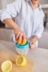 A person is squeezing a lemon using a juicer in a sunny kitchen. Fresh lemons sit on the counter, and the kitchen looks inviting and clean.