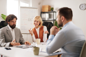 Three team members engage in a discussion at a conference table in an office. They share ideas and review materials, seeking solutions to challenges.