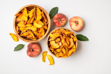 Dried peach slices in wooden bowl and fresh peaches on light background. Organic tasty sweet dried fruit, healthy dessert, vitamins and fiber. Food background, snack vegan flat lay top view