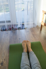 Top view of womans legs. Woman practicing yoga in living room on green sports mat