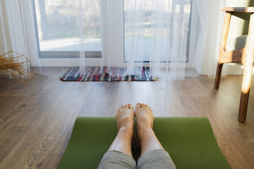 Top view of womans legs. Woman practicing yoga in living room on green sports mat