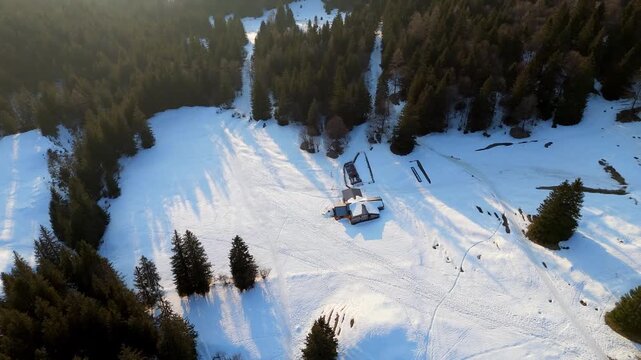 Aerial drone view of a snowy mountain chalet at sunset in Val di Scalve, Orobie Alps. Cozy winter cabin near Presolana peak in golden light