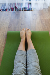 Top view of womans legs. Woman practicing yoga in living room on green sports mat
