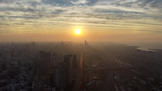 Slow drone pan shows Buenos Aires skyline at sunrise, with the sun rising over the R&iacute;o de la Plata and warm haze backlighting high‑rise towers and rail yards in the south‑eastern, Argentina