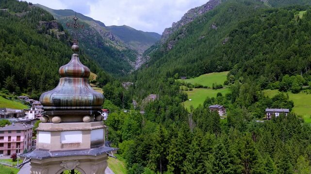 aerial close up to a village church in Val di Scalve, Orobie Alps. Scenic Italian mountain town with bell tower and majestic rocky peaks in the background