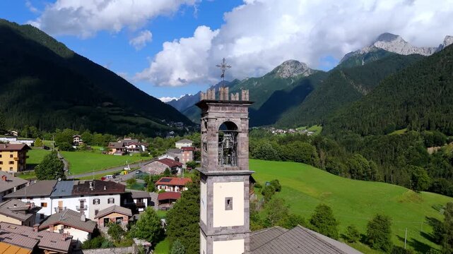Cinematic drone orbit around a church bell tower in Val di Scalve, Orobie Alps. Scenic Italian mountain village and valley landscape in the background