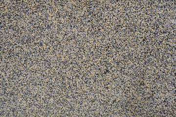 A close-up shot captures the rough, granular texture of a wall coating made of small, multi-colored grains of yellow, gray, and black