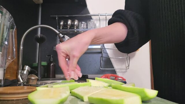 Woman salting and rinsing sliced green chayote for cooking. Food preparation, culinary process.