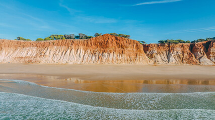 Aerial view of the golden sands meeting the towering cliffs, where the blue sky kisses the ochre earth, Praia da Falesia, Faro District, Algarve, Portugal.