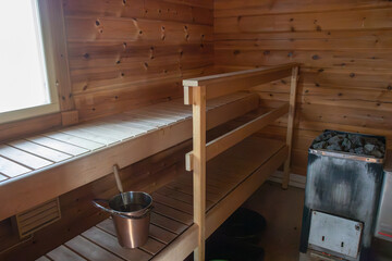 Interior of a traditional Finnish sauna with wooden benches, walls, and a basket of water. Warm, cozy atmosphere highlighting Nordic culture, relaxation, and wellness