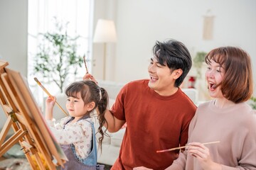 Fototapeta premium Family enjoys painting together in a bright room with natural light and a large easel for creative fun on a sunny day