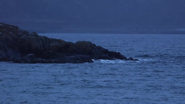 Dark blue waves crashing on black rocks in Teriberka during twilight. Moody and dramatic arctic seascape of the Barents Sea
