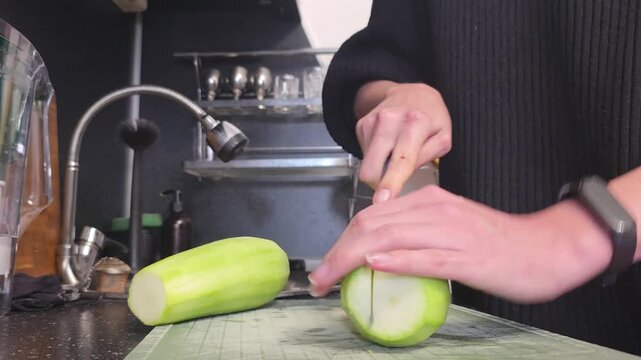 Woman slicing green winter melon into wedges on a cutting board in a kitchen during food preparation for cooking