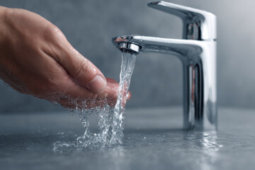 A hand under a modern chrome faucet with flowing water, dark creaturestrating handwashing hygiene in a bathroom or kitchen setting