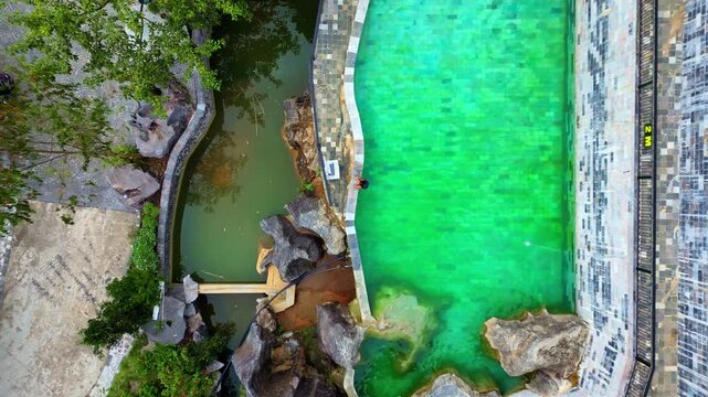 Aerial view of a person on a vivid emerald pool contrasting with a dark stream surrounded by lush greenery, creating a serene oasis, Ha Giang, Ha Giang, Vietnam.