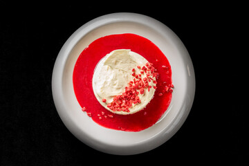 A close-up, high-angle studio shot of a gourmet white cheesecake with a cookie crust, topped with raspberry coulis and freeze-dried raspberries on a modern white plate