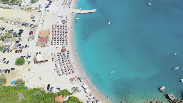 Aerial view of vibrant turquoise waters meeting the light sand beach lined with colorful umbrellas, creating a stunning contrast, Himare, Vlore County, Albania.