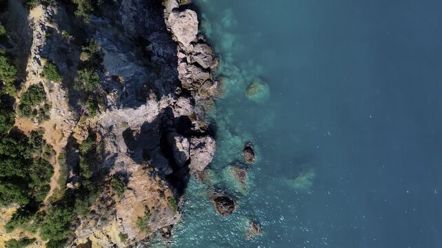 Aerial view of the rugged coastline where jagged rocks meet the turquoise sea, creating a stunning contrast of textures and tones, Himare, Vlore County, Albania.