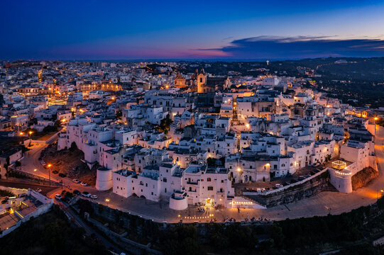 Aerial view of the enchanting white-washed architecture of Ostuni glows softly under the twilight sky, Puglia, Italy.