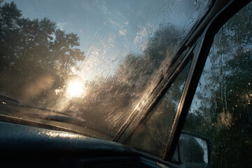 Fototapeta premium Close-up view of a car windshield with raindrops and water streaks during rainy weather at sunset