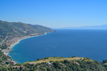 Taormina coastline with Mediterranean sea and blue sky.  Scenic view of the urbanized coastline meeting the blue Ionian Sea under a clear sky.