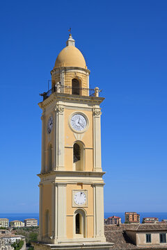 Torre dell'Orologio clock tower in Rossano, Calabria, Italy. Historic yellow clock tower standing against a clear blue sky with a glimpse of the sea.