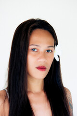 Studio headshot of confident woman with red lipstick and white flower in hair, beauty portrait on white background
