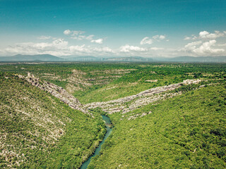 Aerial view of the vibrant green river snaking through the rugged canyon, contrasting against the distant hazy mountains, Krka national park, Sibenik-Knin County, Croatia.