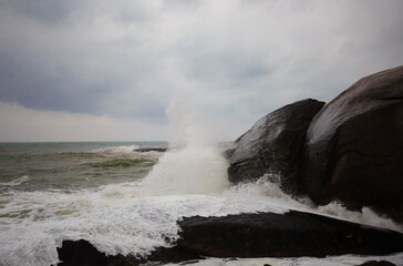 Under a cloudy sky, the waves crashed against the massive rocks, creating huge surges. (Scenic view of Hainan Stone Park, China)