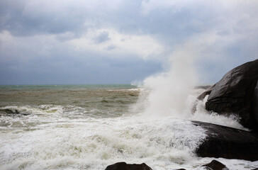Under a cloudy sky, the waves crashed against the massive rocks, creating huge surges. (Scenic view of Hainan Stone Park, China)