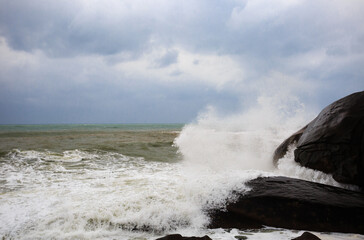 Fototapeta premium Under a cloudy sky, the waves crashed against the massive rocks, creating huge surges. (Scenic view of Hainan Stone Park, China)