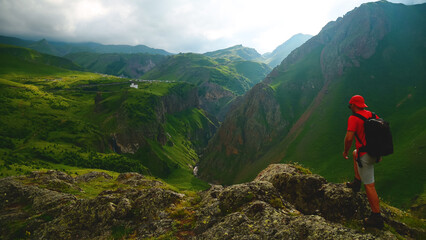Obraz premium a backpacker in the mountains on top of a peak looks down at a gorge