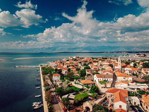 Aerial view of the charming town with its red-tiled roofs nestled against the tranquil azure sea, a striking contrast under the vast blue sky, Nin, Zadar County, Croatia.