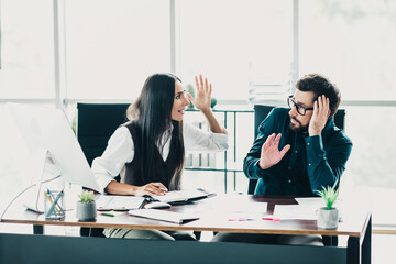 Business partners discuss at a modern loft office with a gesturing woman and listening man in a busy collaborative workspace