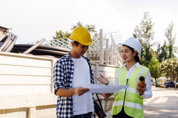 Asian construction workers, a man and a woman, collaborating on a building project, reviewing plan outdoors