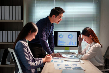 Male manager scolding two stressed female employees during a late meeting at the office, causing pressure and feeling overworked