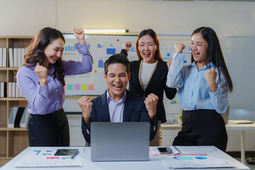 Obraz premium Happy Asian business team celebrating success in the office, cheering and raising fists, showing concept of goal achievement
