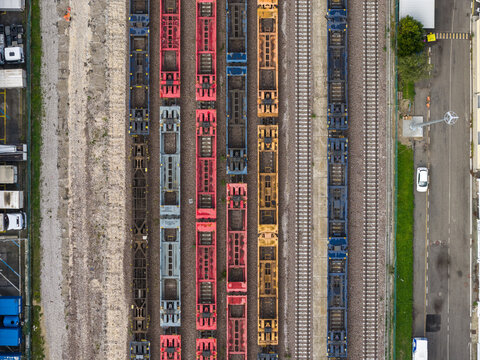 Aerial view of colorful train cars lined up in neat rows, creating a striking geometric pattern of steel and gravel, Trieste, Italy.