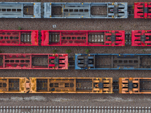 Aerial view of colorful train cars parked on parallel tracks, a geometric dance of steel and hues, contrasting with the earthy tones of the gravel, Trieste, Italy.