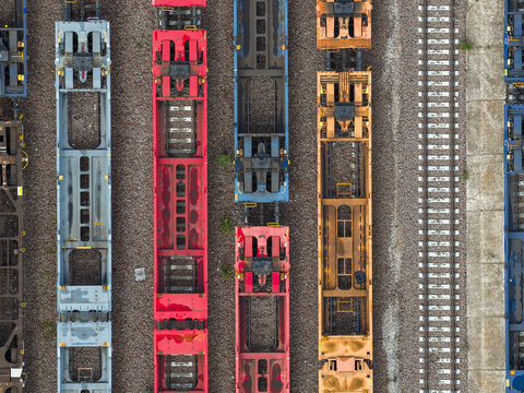 Aerial view of colorful train cars parked along the tracks, a geometric tapestry of rust, red, blue, and yellow in the industrial heart, Trieste, Italy.