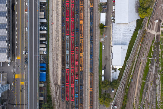 Aerial view of trains lined up in vibrant hues of red and blue, contrasting sharply with the gray concrete and asphalt, Trieste, Italy.
