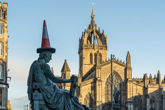 View of David Hume statue humorously adorned with a traffic cone in front of the majestic St Giles' Cathedral on a sunny day, Edinburgh, Edinburgh, United Kingdom.