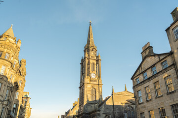 View of golden sunlight kissing the ancient stone facades and the soaring spire of a historic church in the old town, Edinburgh, Scotland, United Kingdom.
