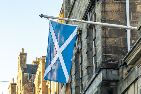 View of the Saltire flag waving proudly against the backdrop of aged stone buildings under a soft blue sky, Edinburgh, Old town, Scotland, United Kingdom.