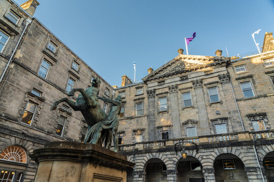 View of the bronze sculpture of Alexander and Bucephalus in front of the city hall building with flags fluttering against a clear sky, Edinburgh, Scotland, United Kingdom.