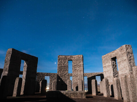 View of stark, grey monoliths rise against a deep blue, star-speckled sky, a modern echo of ancient mysteries, Stonehenge Memorial, Goldendale, Washington, United States.