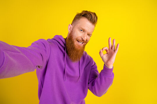 Young bearded man in purple hoodie smiles and poses for a fun self portrait against a bright yellow background capturing happiness and style - Powered by Adobe