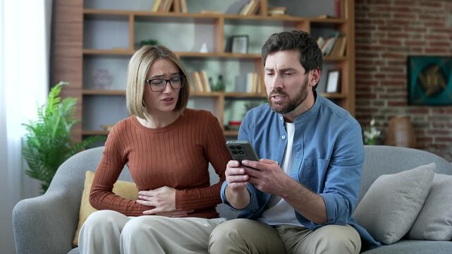 Sick woman suffering from stomach pain at home. Husband supports his wife and uses an app on phone for online medical consultation, telemedicine for medical advice and virtual сounseling or AI therapy