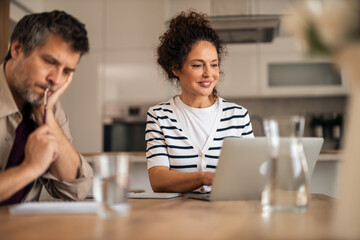 Woman Working on Laptop at Kitchen Table with Thoughtful Partner Nearby