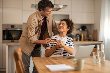 Casual Couple Sharing a Moment at Home Kitchen While Using Laptop and Card